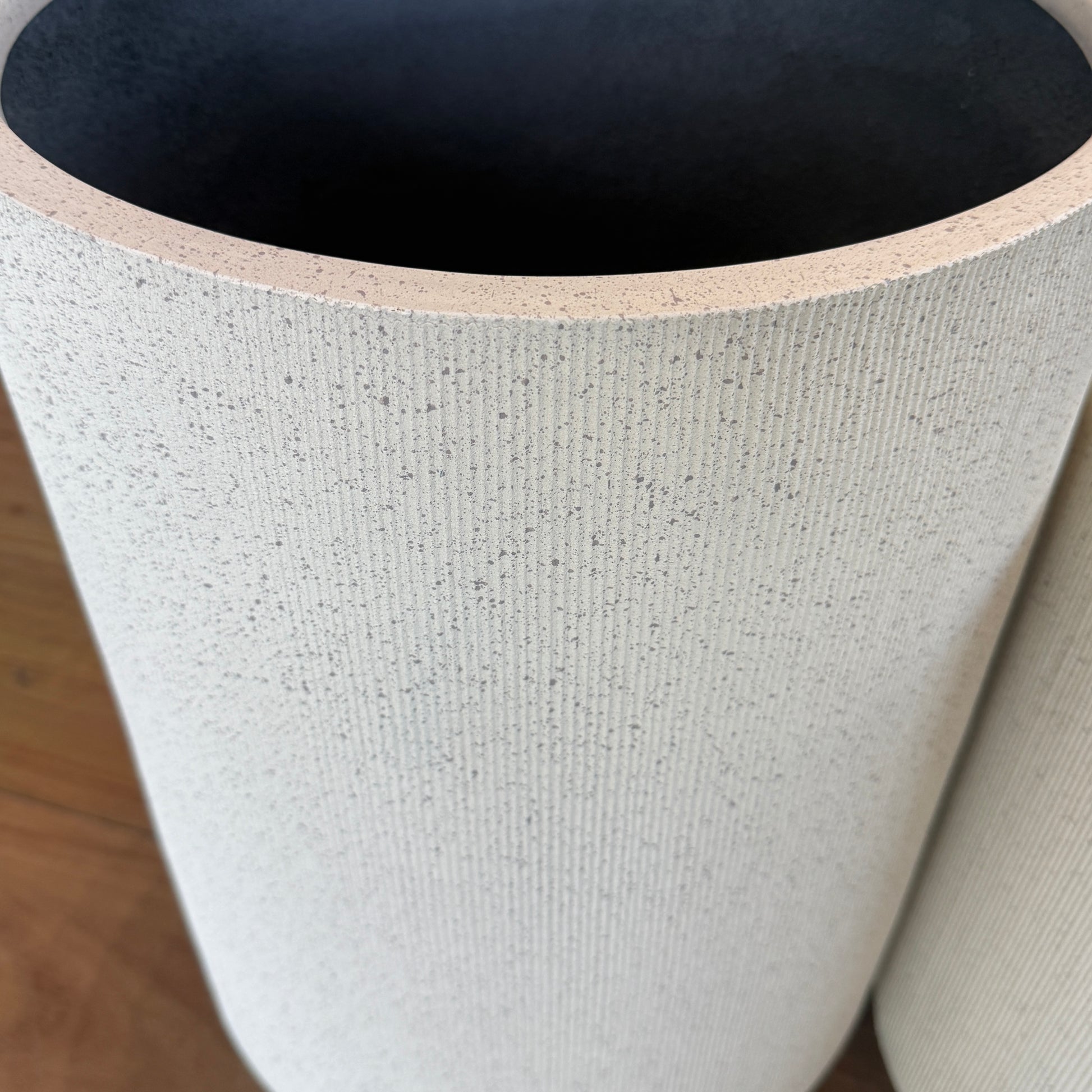 Close-up of a textured cylindrical object with a dark interior on a wooden floor.